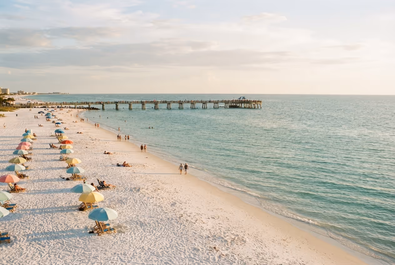 Faixa larga de areia branca de Clearwater Beach com guarda-sóis alinhados e o píer de madeira ao fundo