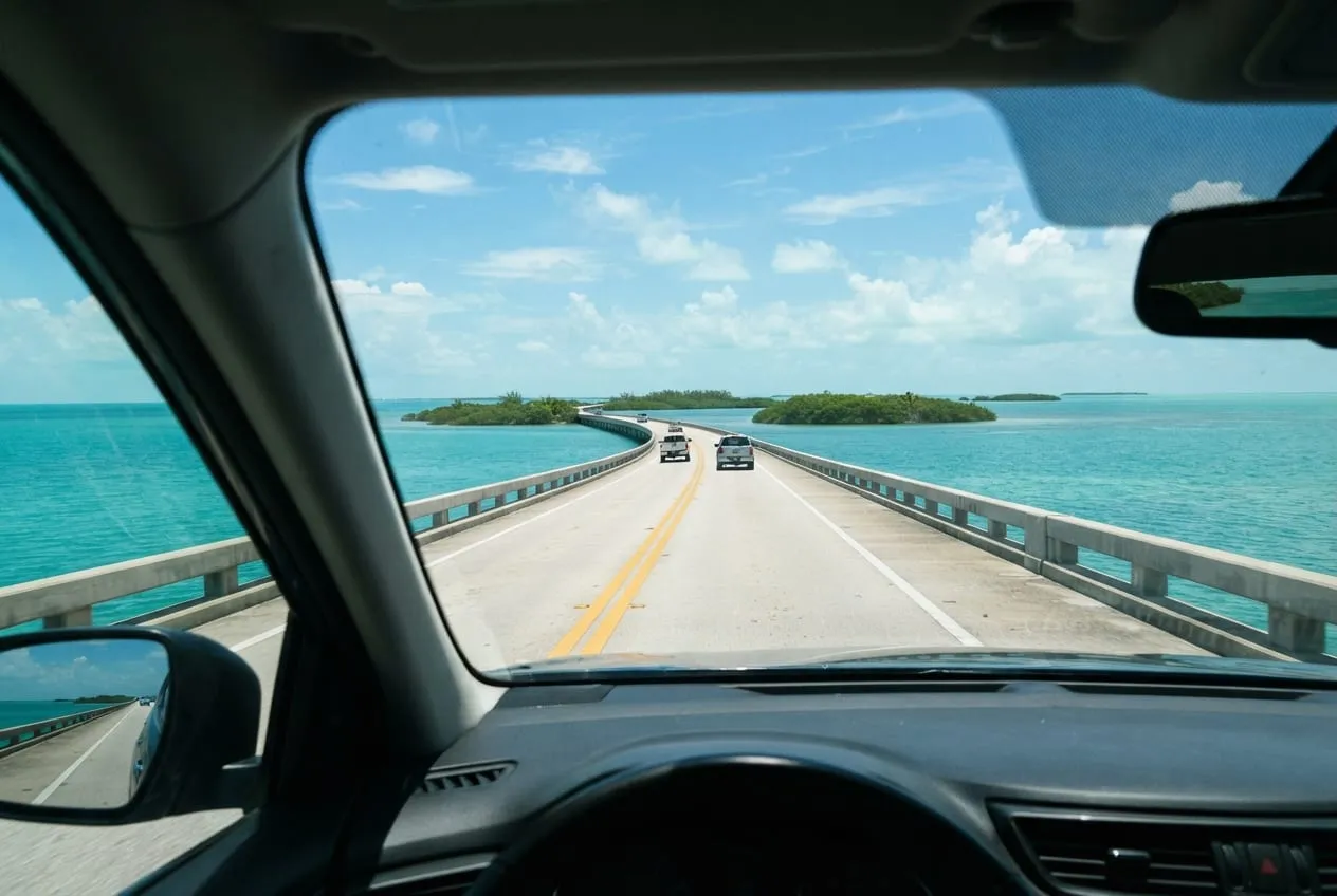 Vista do motorista na Overseas Highway, a pista correndo rente à água turquesa entre ilhotas verdes
