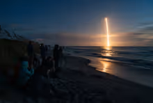 Rastro de fumaça de foguete subindo sobre o horizonte visto de uma praia da Space Coast ao entardecer